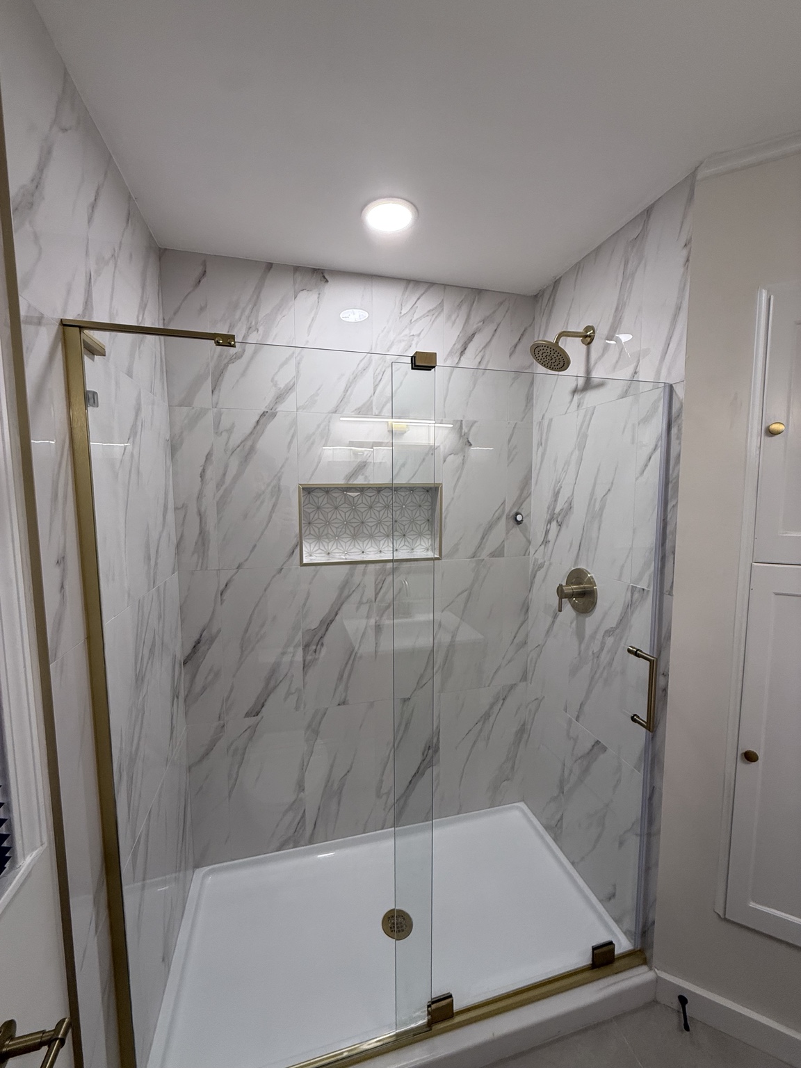 Shower with white marble-style wall tile, a patterned niche, glass enclosure, and brushed gold hardware